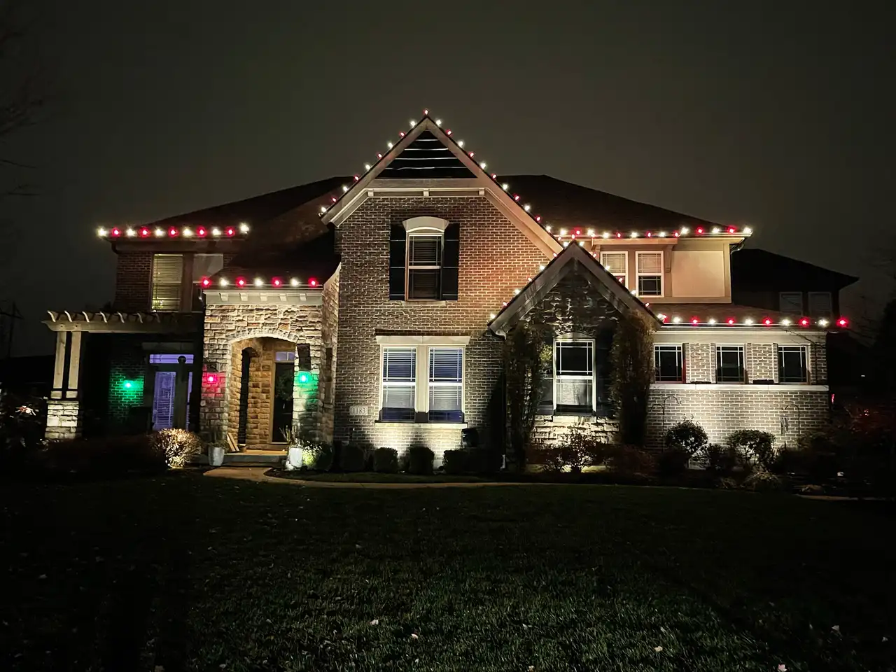 Brick and stone home in the Cincinnati area at night with red and warm white Christmas lights along the rooflines and gables